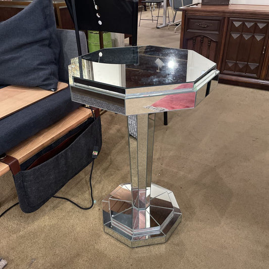 Hexagonal mirrored side table in a room with furniture and carpet.