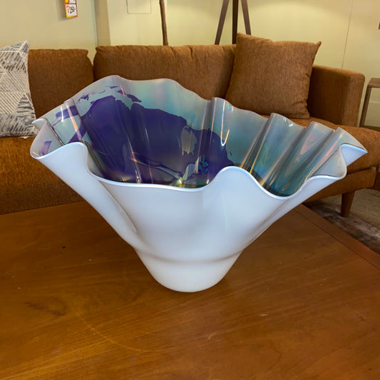 Glass bowl with wavy design on a wooden table, with a couch and pillows in the background.