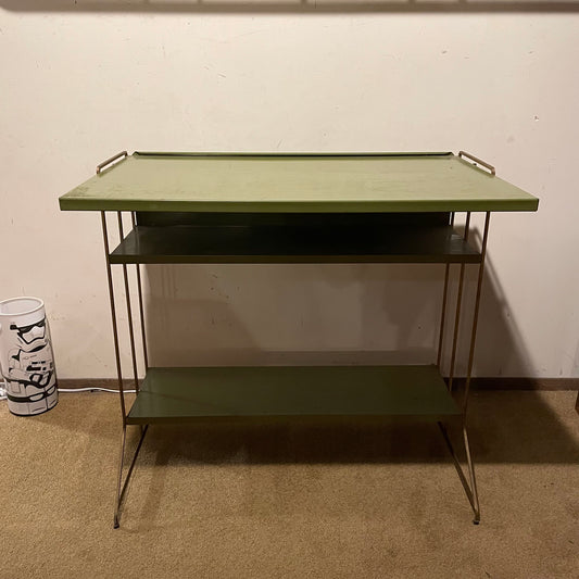Green metal table with two shelves against a white wall.