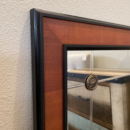Wooden-framed mirror with decorative center on a textured wall