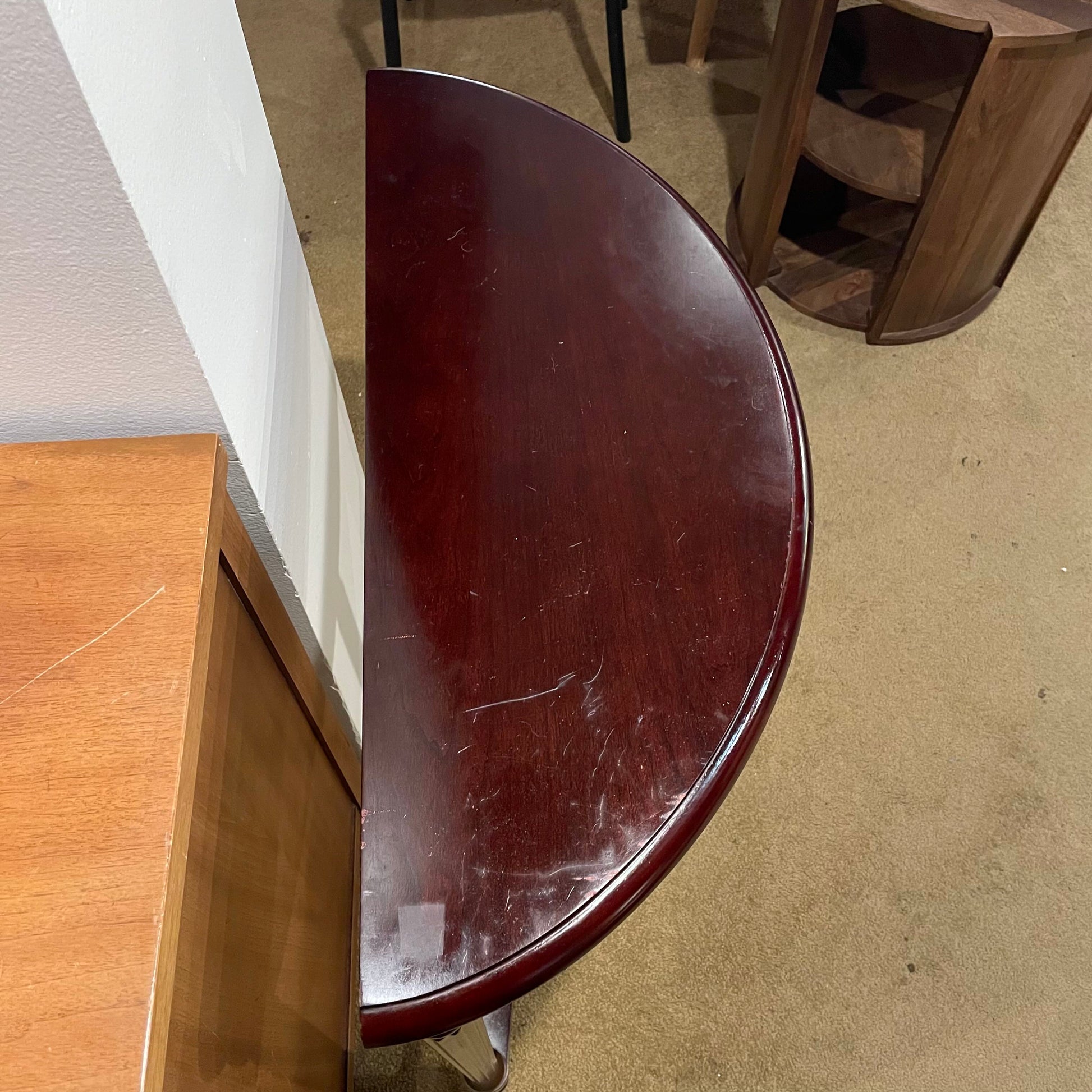 Half-circle wooden table with a worn surface on a carpeted floor.
