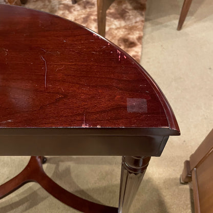 Close-up of a wooden table with visible wear and tear on a carpeted floor.