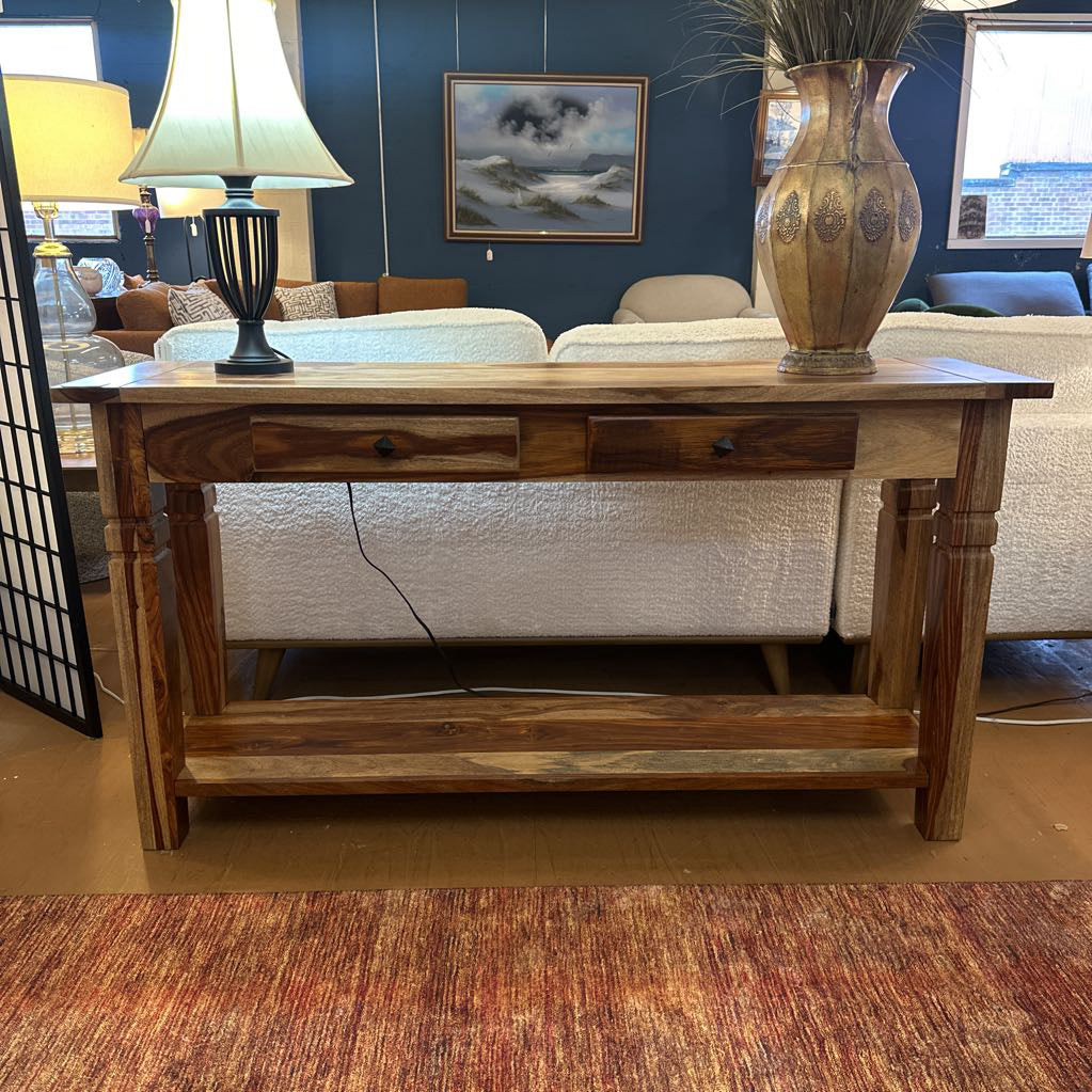Wooden console table in a living room setting with a lamp and vase on top.