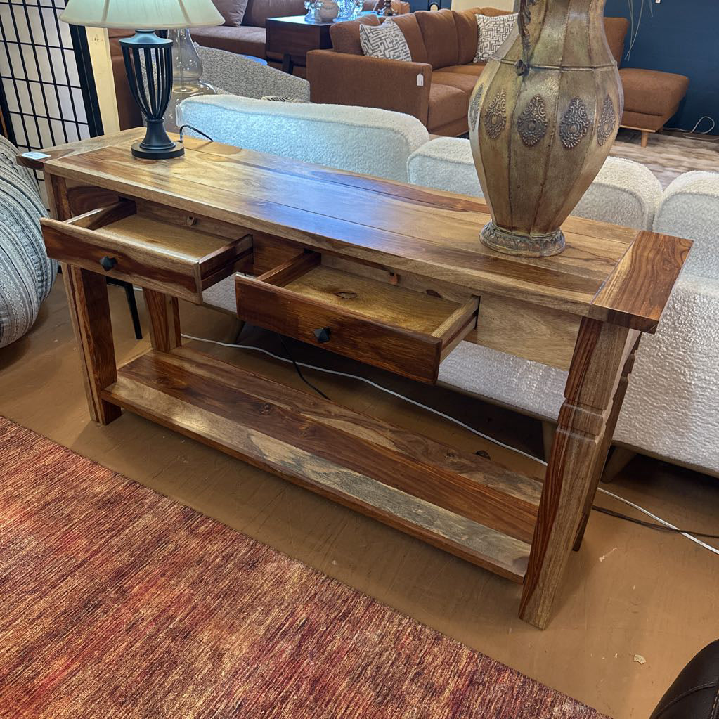Wooden console table with drawers and a vase on top, in a living room setting.
