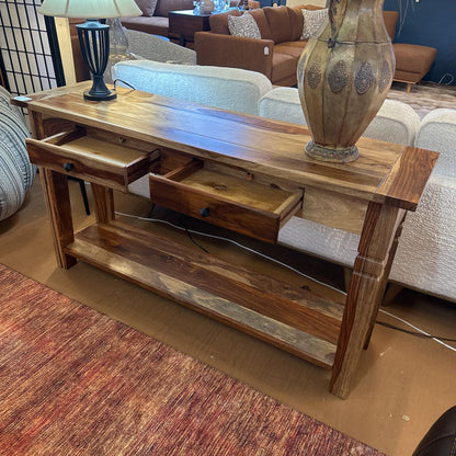 Wooden console table with drawers and a vase on top, in a living room setting.