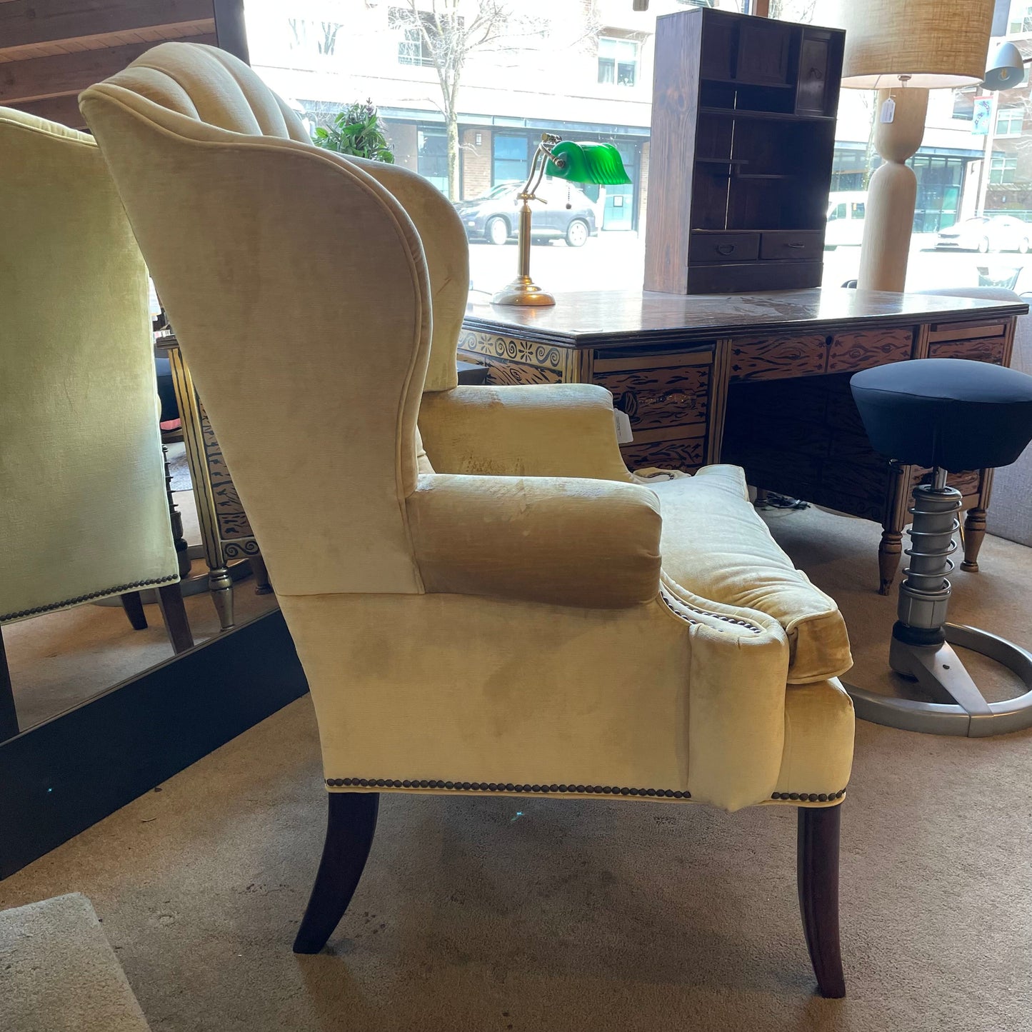 Beige wingback chair in a room with a desk and lamp.