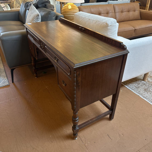 Wooden desk in a room with furniture including a sofa and chairs.