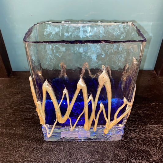 Decorative glass vase with blue liquid and gold wavy patterns on a wooden surface.