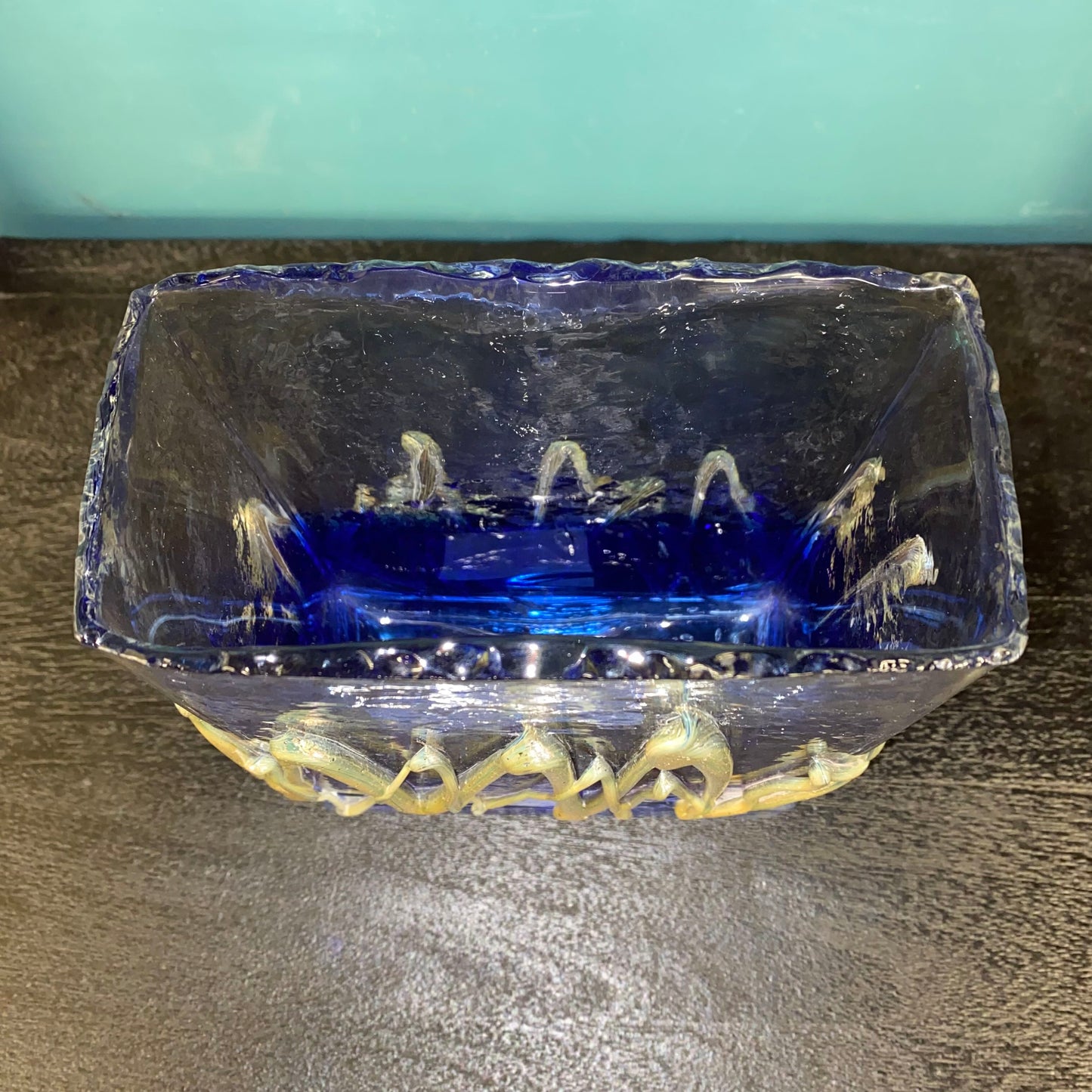 Decorative glass bowl with blue interior and gold exterior on a dark surface