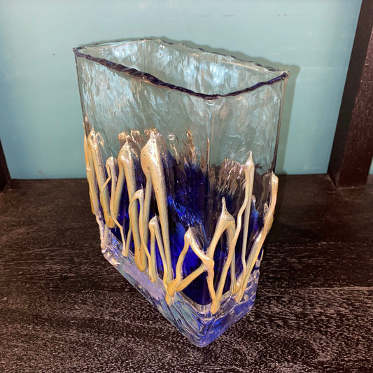 Glass vase with blue and gold design on a textured surface