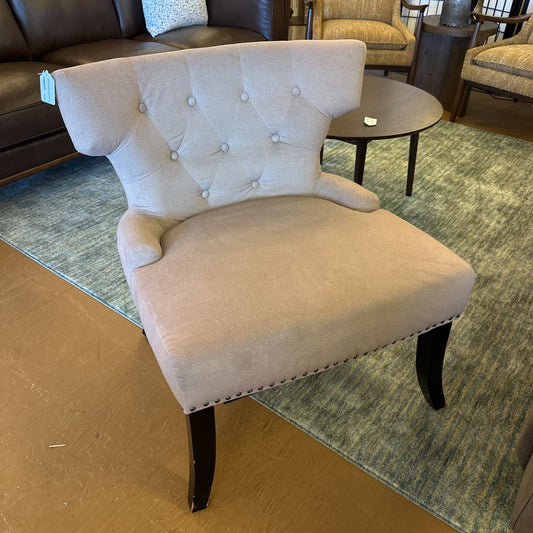 Beige upholstered chair with buttoned backrest in a room setting.