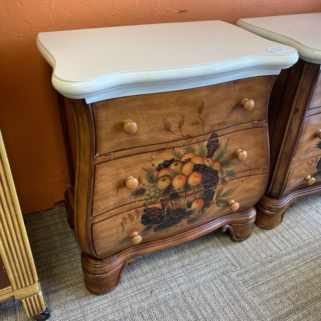Wooden nightstand with fruit design on a textured floor against an orange wall.