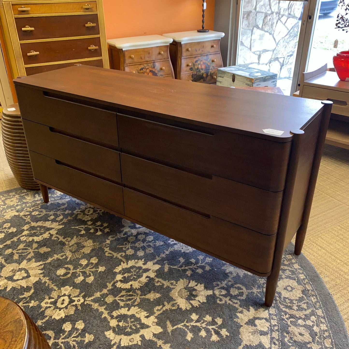 Dark wood dresser on a patterned rug with a room in the background