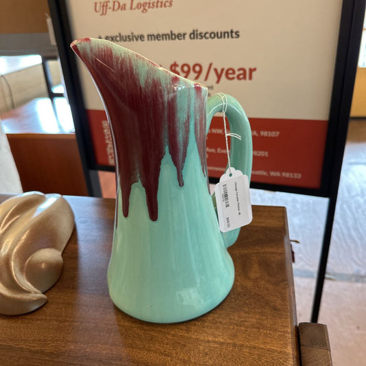 Turquoise pitcher with red accents on a wooden surface, with a blurred background