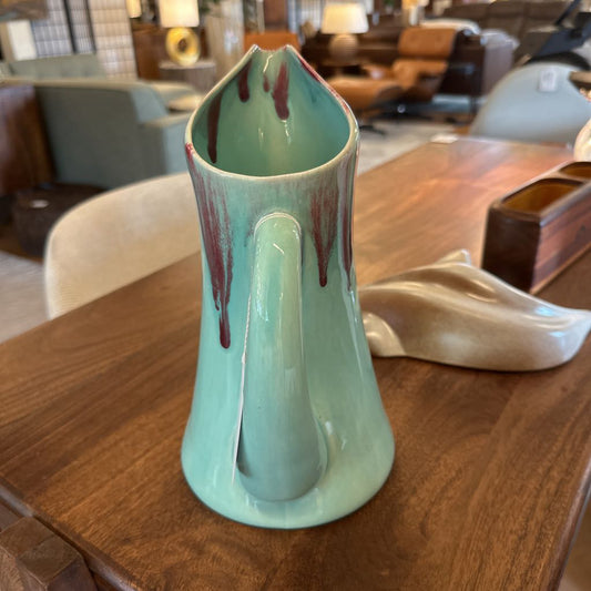 Green ceramic vase with red accents on a wooden table in an indoor setting