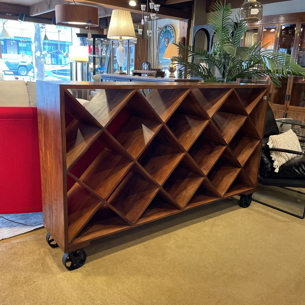 Wooden bookshelf with geometric design on wheels in a room with red walls and plants.