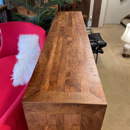 Wooden console table in a room with a pink chair and lamp.