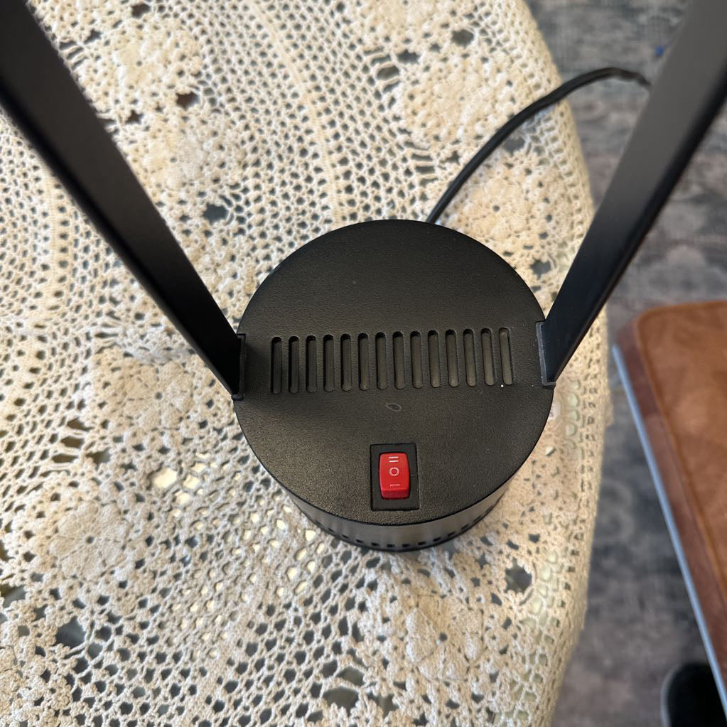 Black outdoor light fixture with red switch on a textured surface