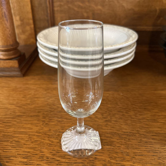 Clear glass goblet on a wooden surface with stacked plates in the background