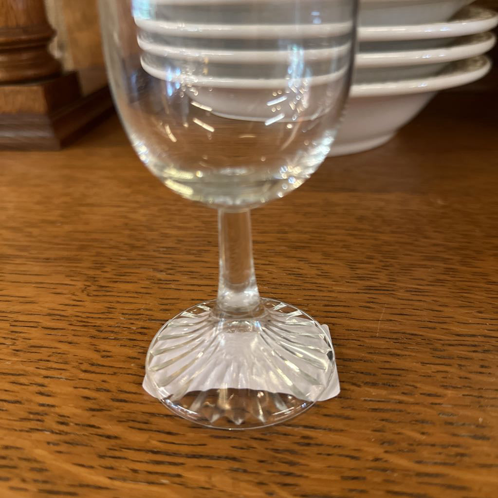 Clear glass goblet on a wooden surface with a stack of plates in the background.