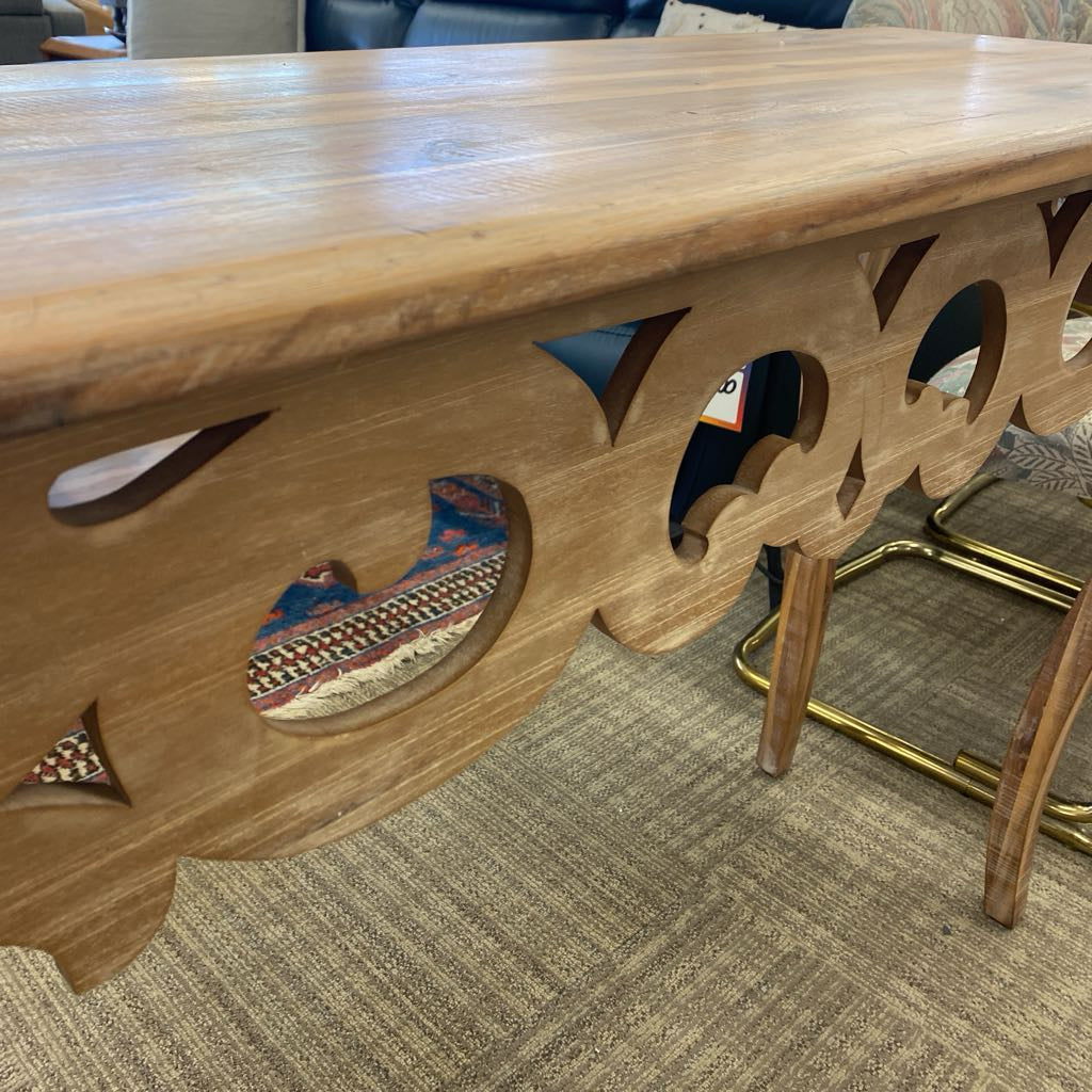 Wooden table with decorative cutouts and inlays on a carpeted floor.