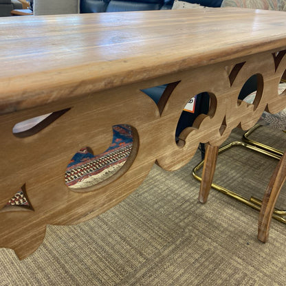 Wooden table with decorative cutouts and inlays on a carpeted floor.