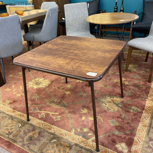 Brown folding table on a patterned rug with chairs around it