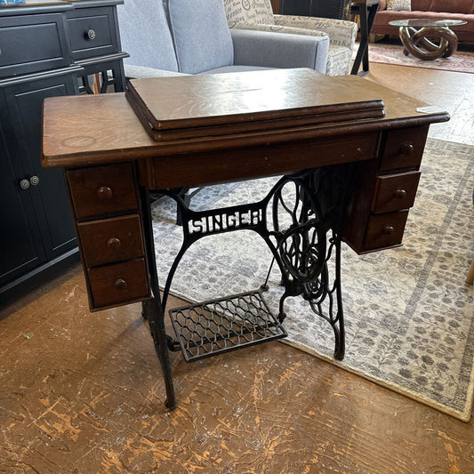 Vintage Singer sewing machine on a wooden cabinet in a room setting.