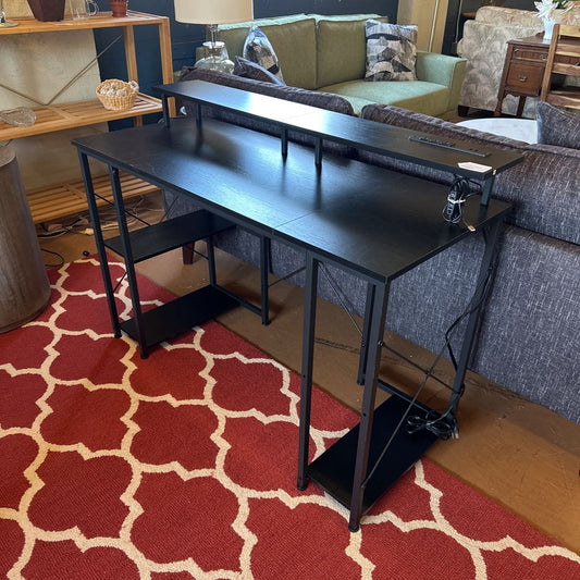 Black adjustable desk in a living room with a red patterned rug.