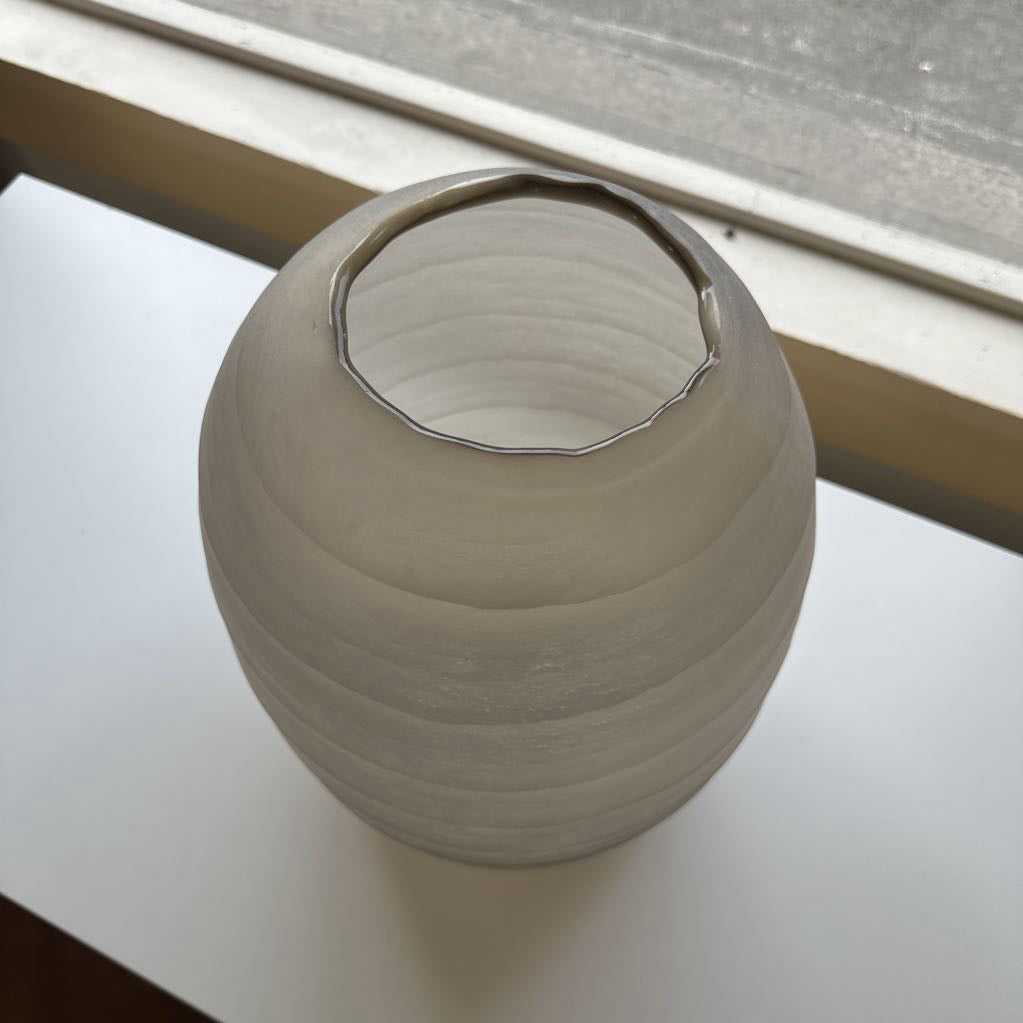 Gray ceramic vase on a white surface with a window in the background
