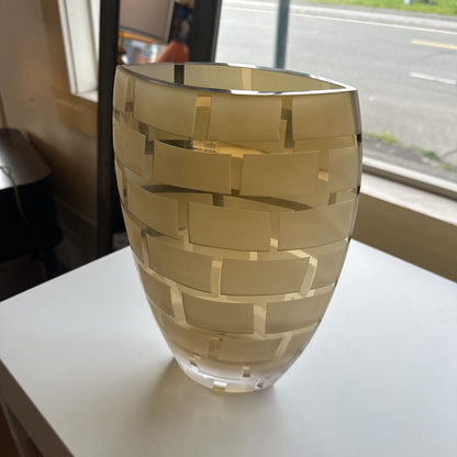 Gold patterned vase on a white surface with a window in the background