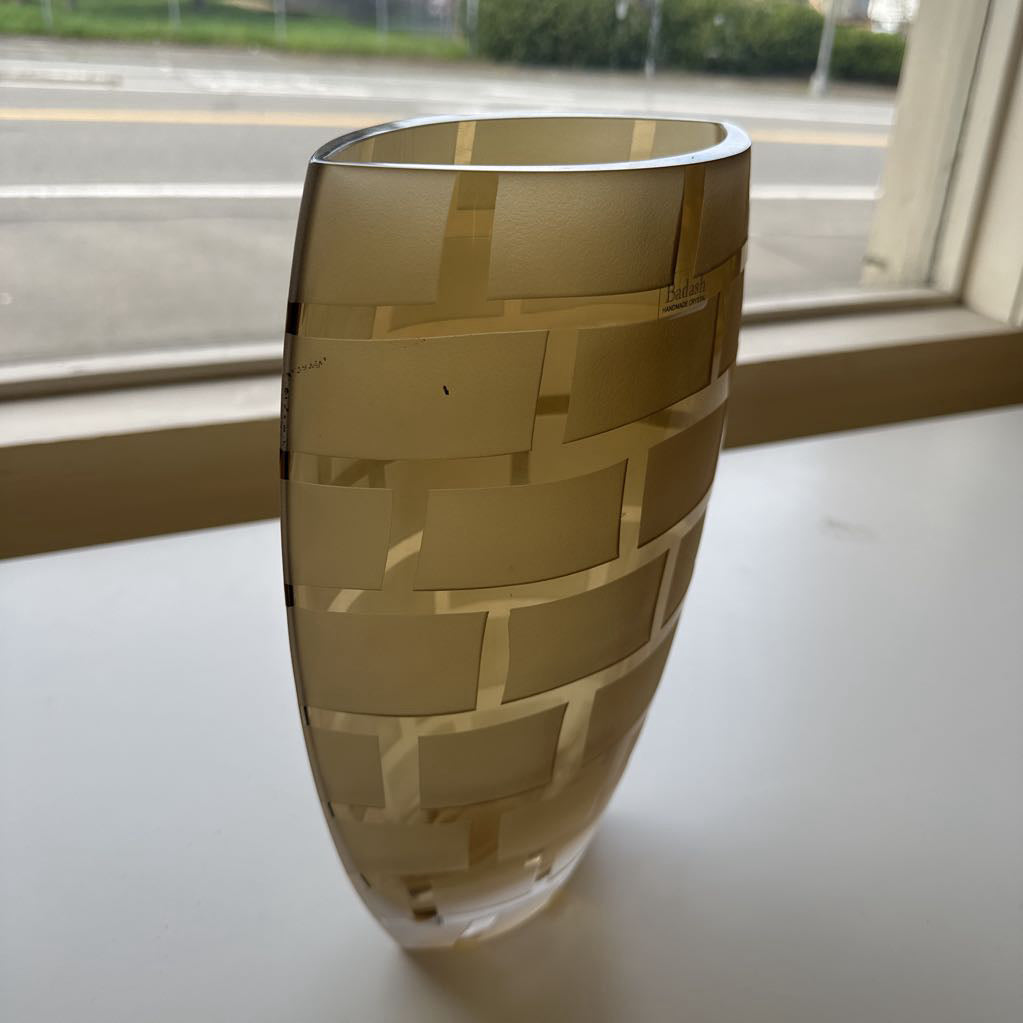 Gold-patterned glass vase on a white surface with a window in the background