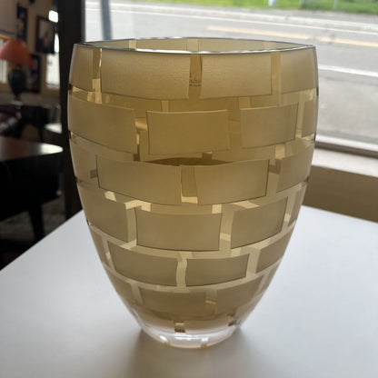 Glass vase with woven gold pattern on a white surface