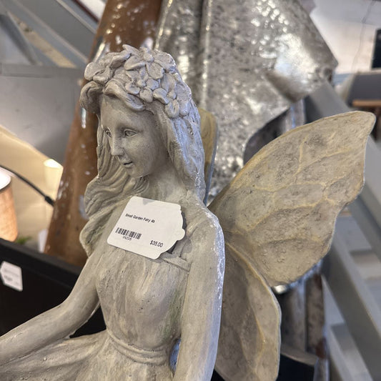Statue of a fairy with a floral headpiece and leaf wings, held by a person in an indoor setting.
