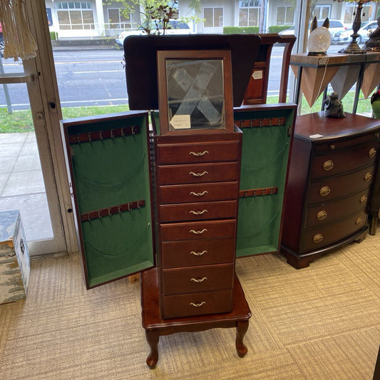 Wooden jewelry armoire with open door showing green interior, displayed indoors.