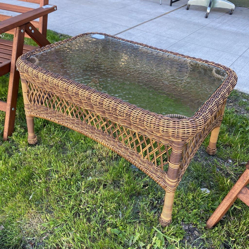 Wicker coffee table with glass top on a grassy outdoor area