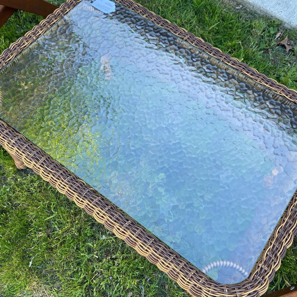 Glass-top coffee table with wicker frame on grass