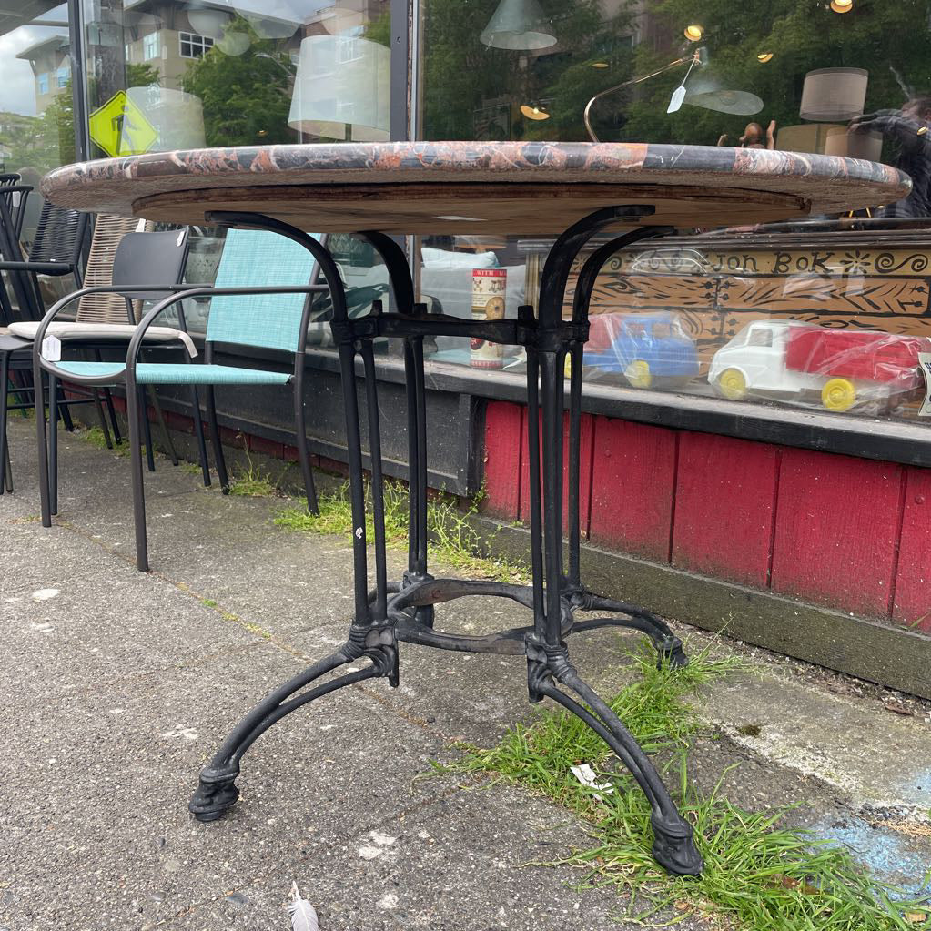 Side view of a round marble-top bistro table with a black cast iron base
