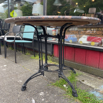 Side view of a round marble-top bistro table with a black cast iron base