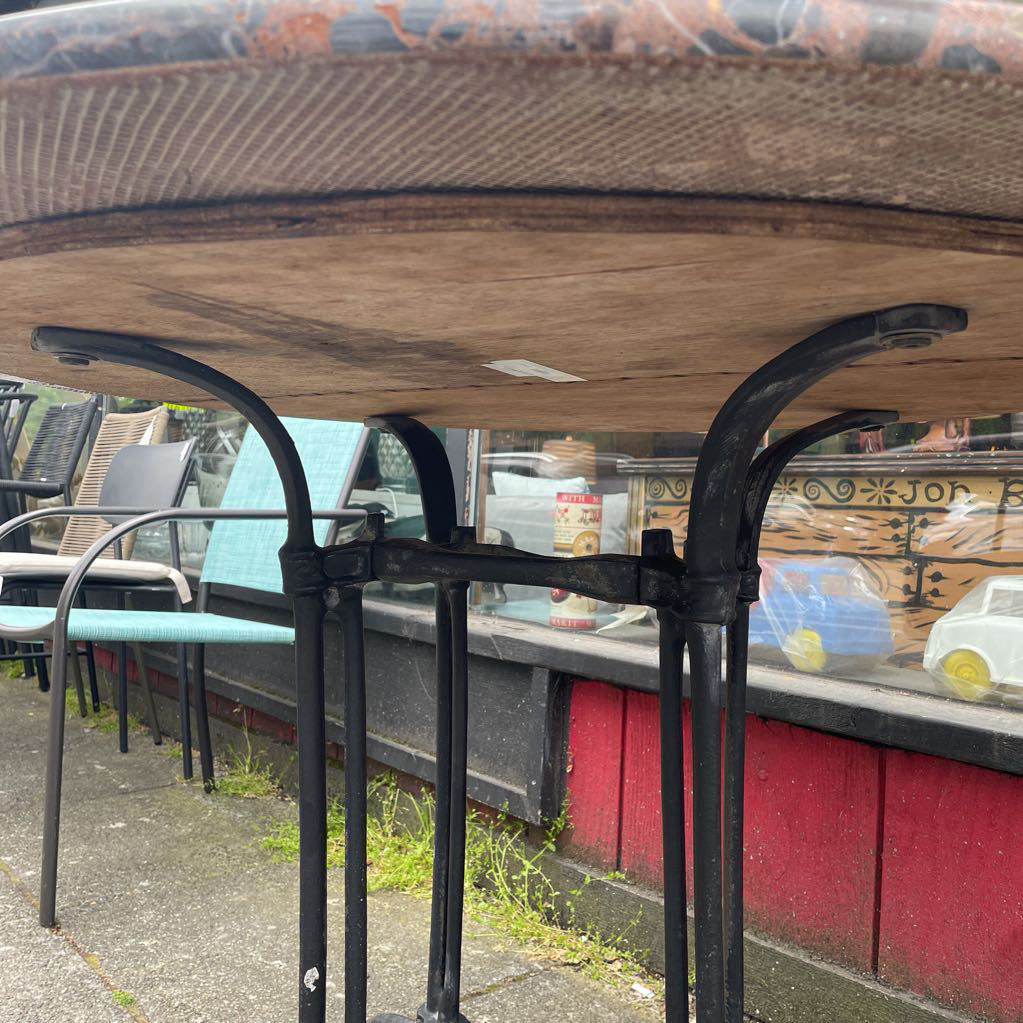 Underside of a round marble-top bistro table showing the wooden support and cast iron base