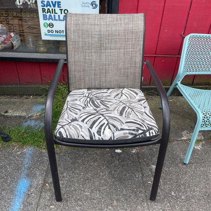 Front view of an outdoor patio chair with a black frame, grey mesh back, and tropical leaf print cushion