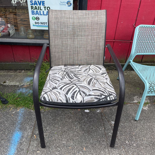 Front view of an outdoor patio chair with a black frame, grey mesh back, and tropical leaf print cushion