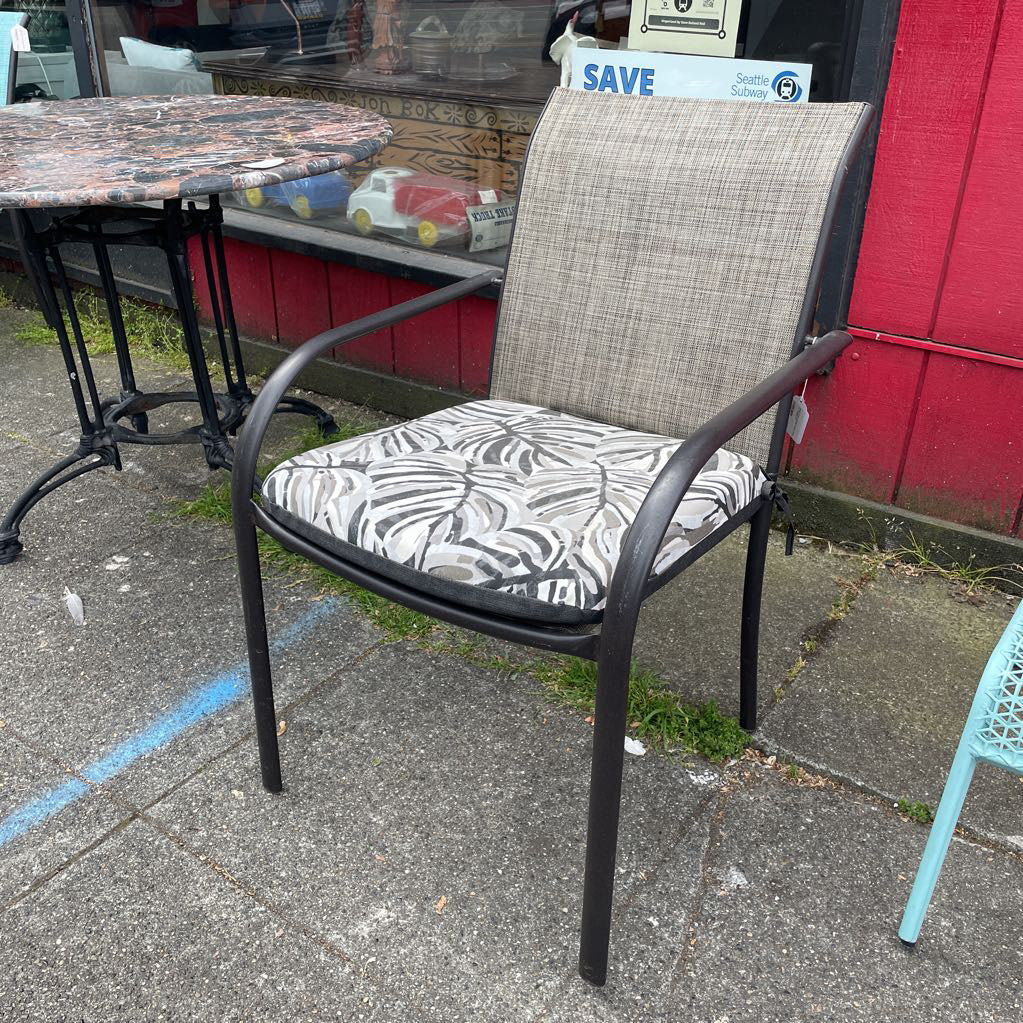 Outdoor patio chair with black frame and grey mesh back, tropical leaf print cushion