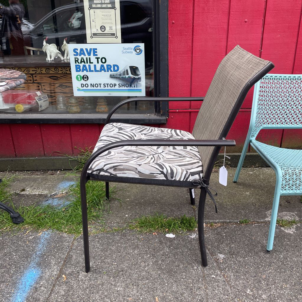Side view of an outdoor patio chair with a black frame, grey mesh back, and tropical leaf print cushion