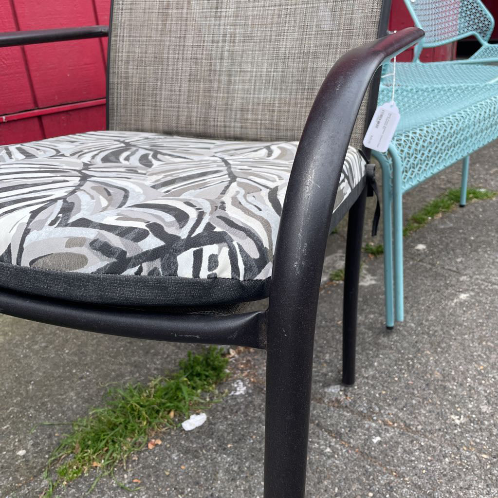 Close-up of the armrest and tropical leaf print cushion of an outdoor patio chair