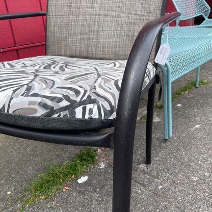 Close-up of the armrest and tropical leaf print cushion of an outdoor patio chair